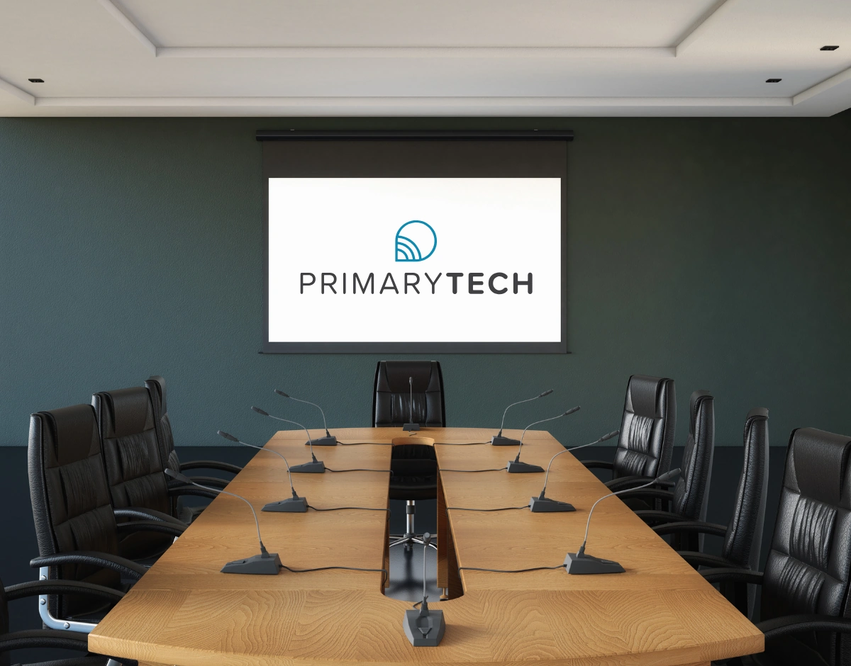 Boardroom with conference microphones and a projector screen displaying the PrimaryTech logo, representing audio visual and meeting room solutions