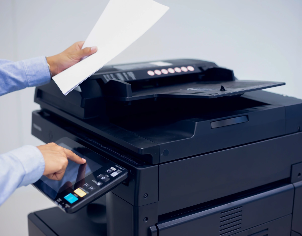 Person using an office multifunction printer touchscreen while collecting printed pages, representing managed print